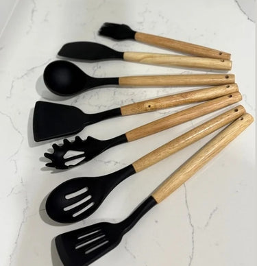 Set of black silicone utensils with wooden handles on a light gray surface